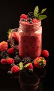Bright mixed berry smoothie in a mason jar with fresh berries and mint garnish.